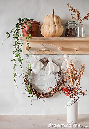 Cozy interior of the hallway. Wooden hanger with flower, pumpkin, grape wreath and homemade paper ghost garland Stock Photo