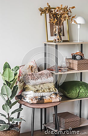Cozy interior of the living room - a chair with a stack of warm blankets, a rack with autumn decor in Scandinavian style Stock Photo
