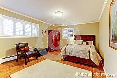 Cozy large guest room with suede brown bed and armor, hardwood floors and beige walls. Stock Photo