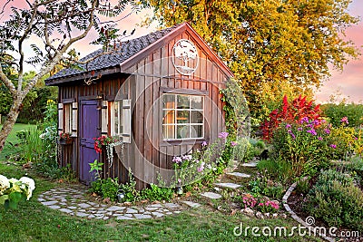 Cozy Little Cottage Garden Shed in Grassy Flower Beds at Sunset Stock Photo