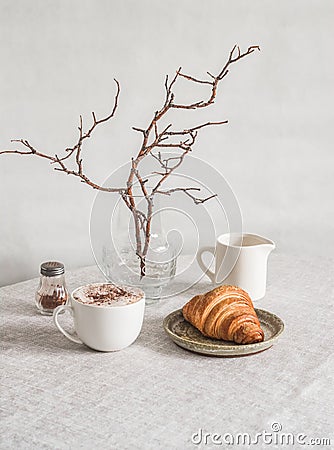 Cozy morning - cappuccino, croissant, vase with branches on the table in a bright cozy room Stock Photo