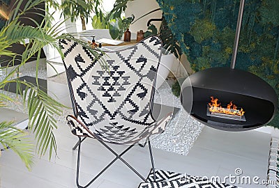 A cozy picnic chair by a hanging fireplace with a ceiling mount. Stock Photo