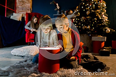 Cozy room decorated in a Christmas style. Beautiful children view a magical gift and prepare for the holiday. Stock Photo