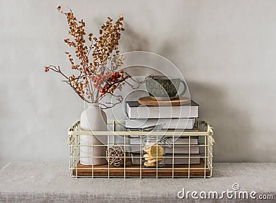 Cozy simple home interior - books in a metal basket, a ceramic cup, dried flowers in a vase on the table. Cozy home interior Stock Photo