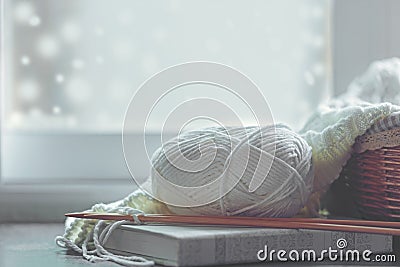 Cozy winter home with warm knitted sweaters and ball of yarn near windowsill, home hobbies, vintage tone. Stock Photo