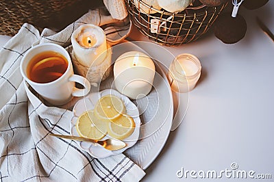 Cozy winter morning at home. Hot tea with lemon, candles, knitted sweaters in basket and modern metallic interior details. Still l Stock Photo