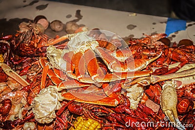 Crab claws and crawdads and shrimp piled on a paper covered cable with ears of corn and onions at a seafood boil - shallow focus Stock Photo