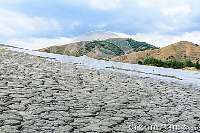 Cracked slope with mud volcano and cloudy sky. Dry land in natural park with muddy volcanoes, dramatic landscape, unique geologic Stock Photo