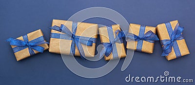 Craft paper wrapped gift boxes in a row on blue background, flat lay with copy space. Christmas abstract banner Stock Photo