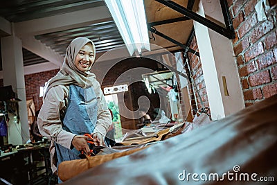 Craftwoman smiling while cutting leather fabric in studio Stock Photo