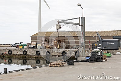 A crane at the harbor to lift fish boxes from boats and up on land, fish boxes stand next to it, a number of euro pallets can be Editorial Stock Photo