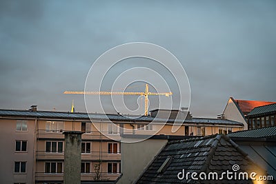 Crane over Munich buildings stands out brightly as setting sun c Editorial Stock Photo