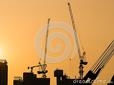 Cranes working at Building Construction site sunset sky Silhouette Industrial background Stock Photo