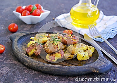 Crash Hot Potatoes, boiled potatoes in a peel, crushed and baked with olive oil and herbs on a wooden plate on a dark concrete Stock Photo