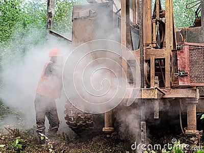 Crawler drilling rig drills well, lot of dust when drilling borehole. harmful labor factors. harmful working conditions Editorial Stock Photo