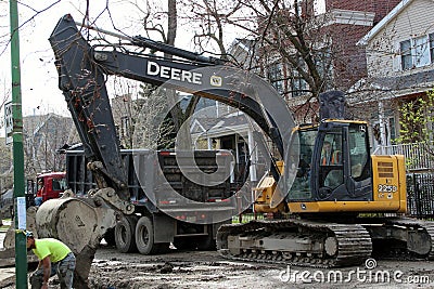 A crawler excavator digs dirt next to a dump truck in Chicago Editorial Stock Photo