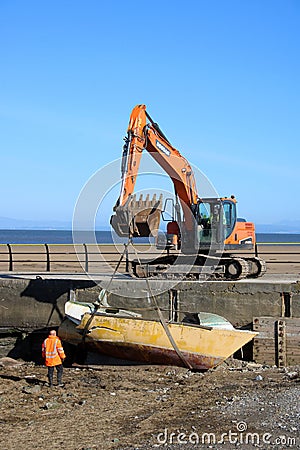 Crawler excavator removing boat wreck from shore Editorial Stock Photo
