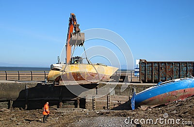 Crawler excavator removing boat wrecks from shore Editorial Stock Photo