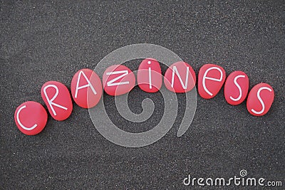 Craziness word composed with red colored and carved stone letters over black volcanic sand Stock Photo