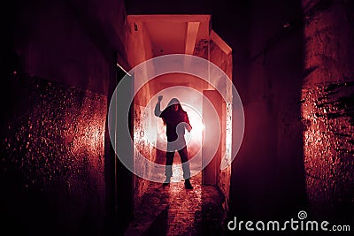 Crazy criminal killer or robber or rapist with knife in hand in dark scary corridor, horror and thriller atmosphere, red toned Stock Photo