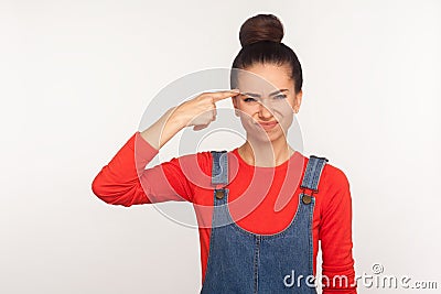 Crazy cuckoo mind. Portrait of girl with hair bun in denim overalls showing stupid gesture and looking with displeased annoyed Stock Photo