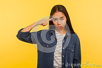 Crazy idea! Portrait of girl in denim shirt showing stupid gesture with finger near head and blaming fool Stock Photo
