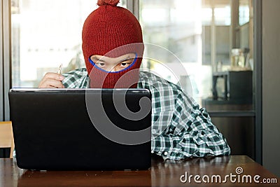 Crazy masked hacker wearing a balaclava with key in hands stealing data from laptop. Internet crime concept. Stock Photo
