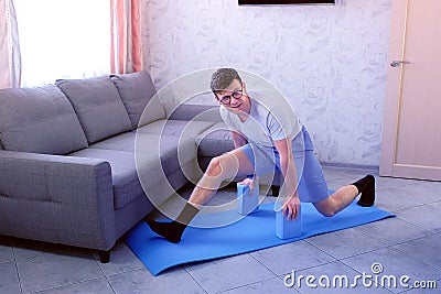 Crazy nerd man is trying to do the splits the first time on the mat at home. Sport humor concept. Stock Photo