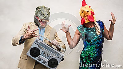 Crazy senior couple dancing at carnival party wearing t-rex and chicken mask - Old trendy people having fun listening music with Stock Photo