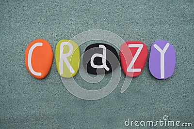 Crazy word composed with multi colored stone letters over green sand Stock Photo