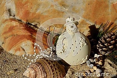 Cream ceramic snowman on beach sand shell pine cone african beads Christmas in July Stock Photo