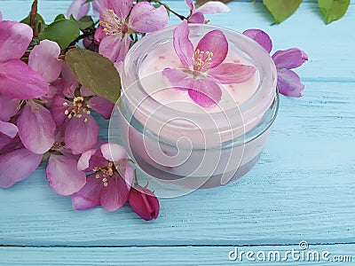Cream cosmetic lotion ointment relaxation moisturizer protection glass essence magnolia handmade pink flowers on blue wooden Stock Photo