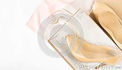 Cream heeled women`s shoes, pink dress and pearls necklace on white background. Stock Photo