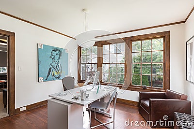 Cream office with brown sofa, work desk, poster and large wooden windows Editorial Stock Photo