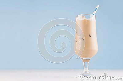 Creamy cold fresh beverage in elegant transparent glass with ice cubes and striped straw in modern light blue interior. Stock Photo