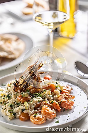 Creamy risotto with orange shrimps and zucchini served with white wine in a restaurant Stock Photo