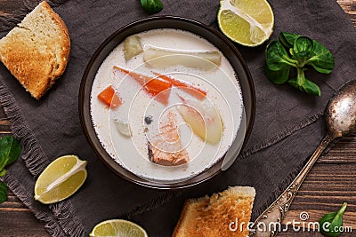 Creamy salmon soup with potatoes and carrots served with toast on a wooden rustic plank table. Finnish fish soup kalakeitto with Stock Photo