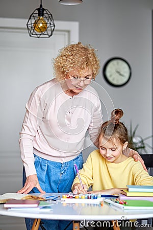 Creative activity. Caring grandma and preteen daughter friends sit at desk Stock Photo