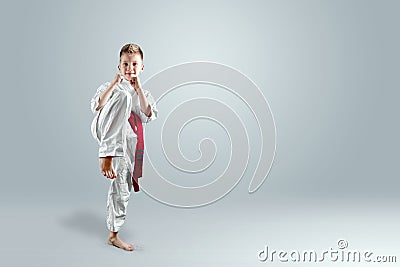 Creative background, a child in a white kimono makes a kick, on a light background. The concept of martial arts, karate Stock Photo