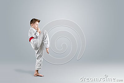 Creative background, a child in a white kimono makes a kick, on a light background. The concept of martial arts, karate Stock Photo