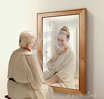 Creative conceptual collage. Smiling senior woman looking in mirror and remembering her past. Young girl in reflection Stock Photo