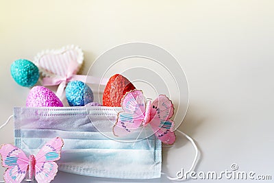 Creative Easter composition of coloful eggs, pink heart, butterflies and medical mask on light background, greeting card Stock Photo