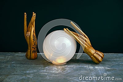 esoteric still life with a ball of predictions and two wooden female hands on concrete table against black wall Stock Photo