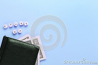 Creative flat lay business concept. Close up of black wallet on a blue background with the words start up of wooden letters. Top Stock Photo