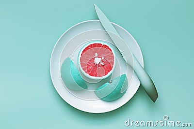 Creative food concept. Turquoise color grapefruit cut on a plate with a knife on turquoise background. Food art Stock Photo