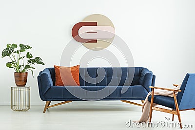 Creative geometric art on a white wall above an elegant blue sofa in a mid-century modern style living room interior. Real photo. Stock Photo