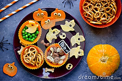 Creative idea for Halloween snack - skull bone dry cereal, cheese ghosts, carrot pumpkin with eyes, cookie and vegetables on plate Stock Photo