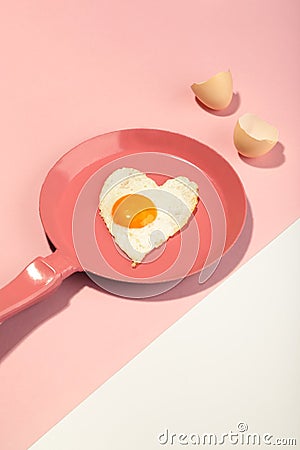 Creative idea with a pink frying pan and egg in heart shape on white and pink background. Minimal food and love concept. Breakfast Stock Photo