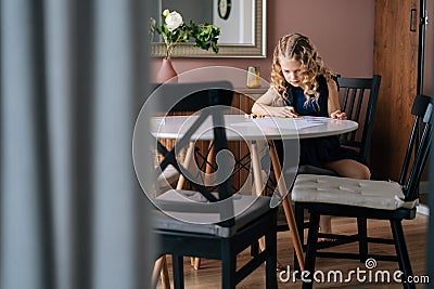 Creative kid girl doing homework at the table in cozy children`s room. Stock Photo