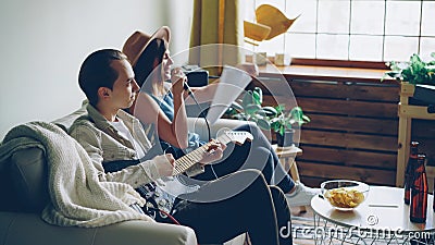 Creative musical duet is practising at home woman is singing in microphone and man is playing the guitar. Young cheerful Stock Photo